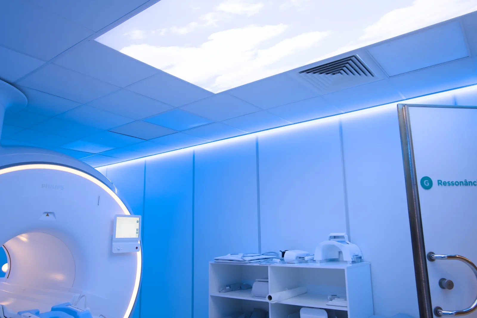 Sala de ressonância magnética da CRMA em luz ambiente azul, com o painel de céu no teto e o equipamento Philips MR 5300