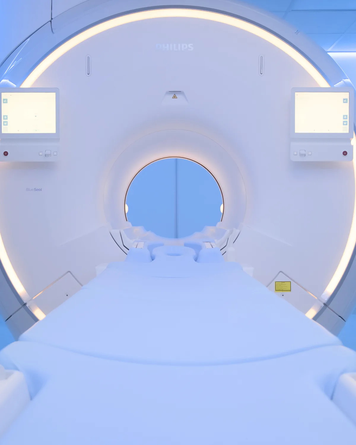 Túnel do equipamento de ressonância magnética Philips MR 5300 da CRMA, visto de frente, com a mesa de exame, o anel de luz âmbar e os ecrãs de apoio